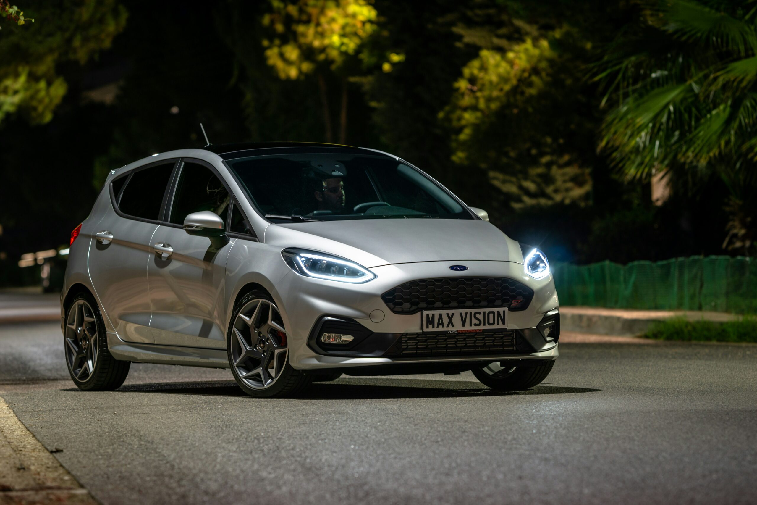 Sølvgrå Ford Fiesta ST med tændte forlygter om aftenen