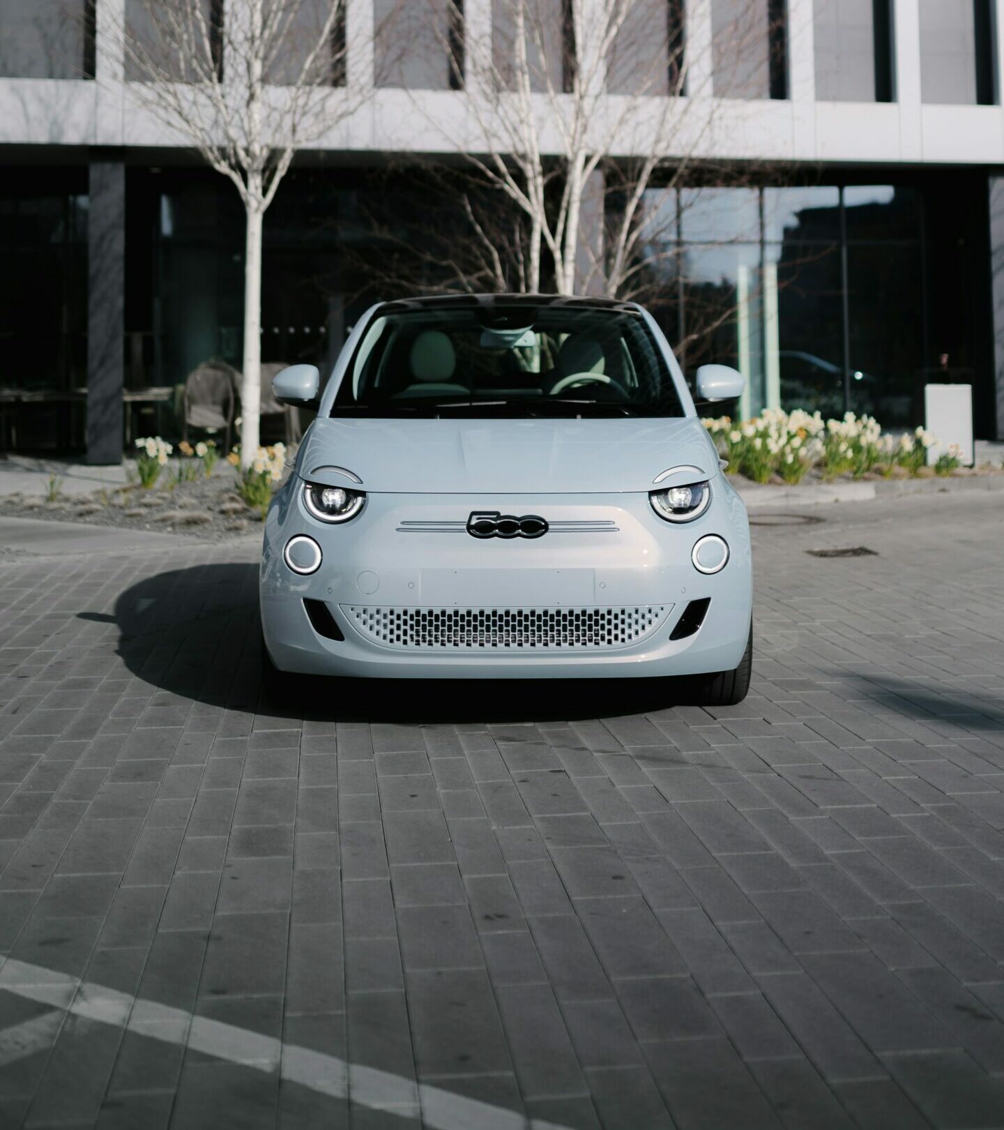 Lysegrå Fiat 500e set forfra foran moderne bygning