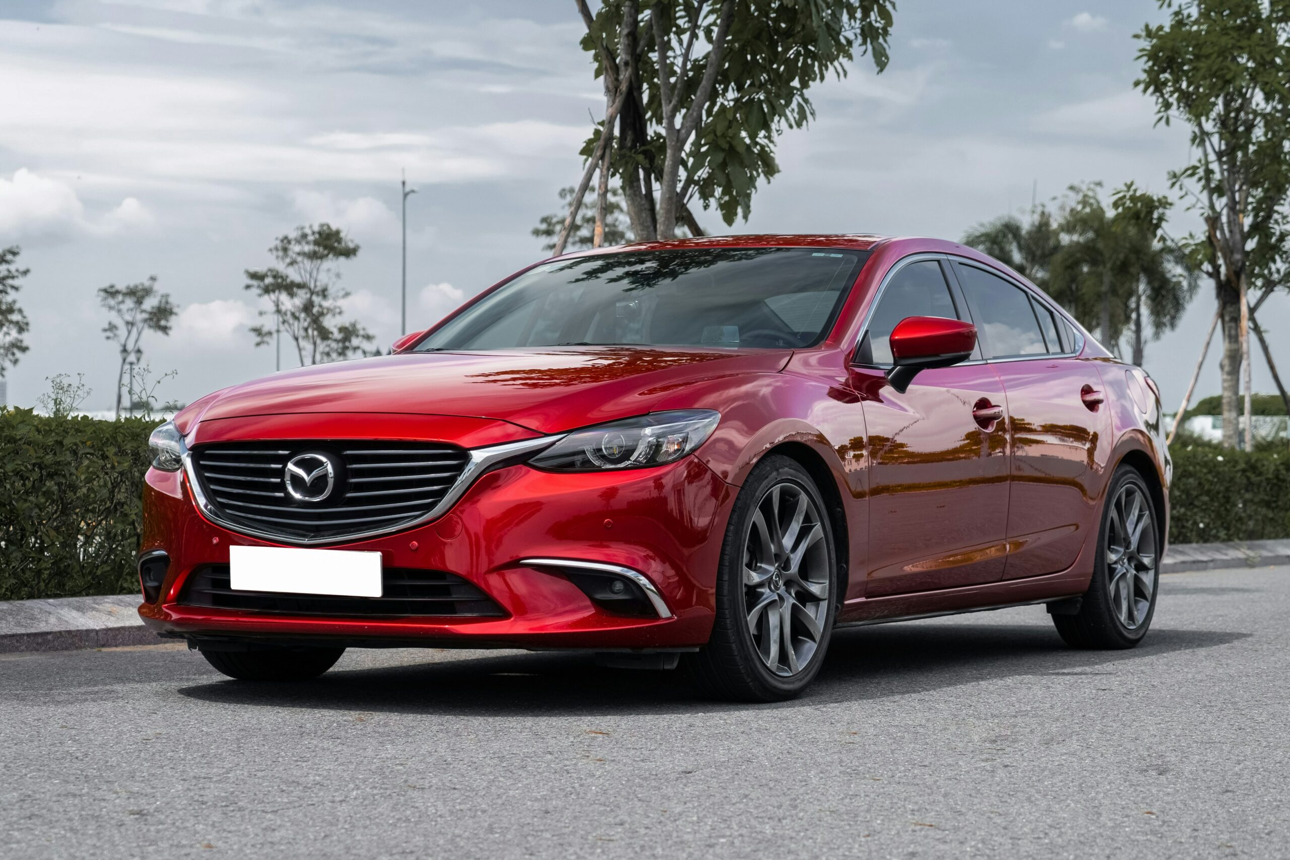 Rød Mazda6 parkeret ved fortov med træer i baggrunden